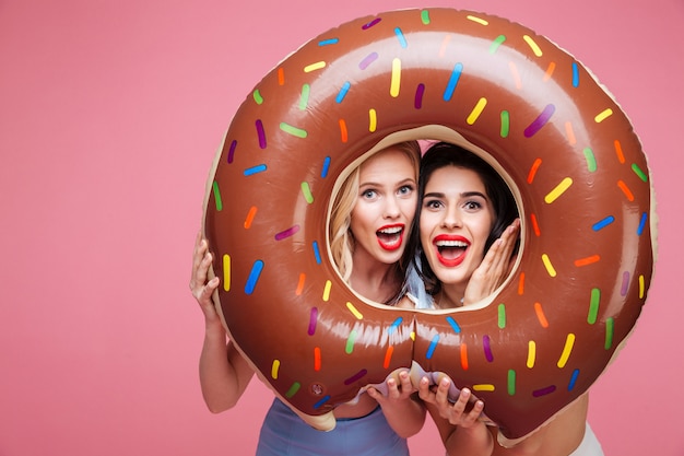 Women in beachwear having fun with donut shaped heart mattress