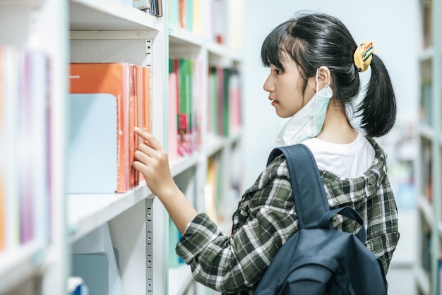 Women carrying a backpack and searching for books in the library.