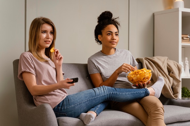 Women on couch watching tv and eating chips