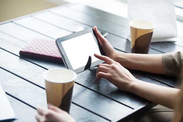 Women hands holding tablet with white blank screen in cafe. Close-up