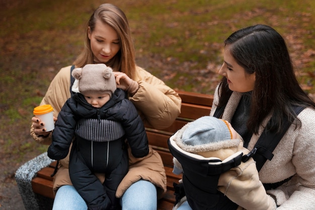 Free photo women holding babies in carriers high angle