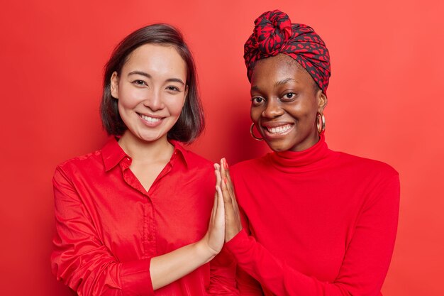 women keep palms pressed together show mutual support and understanding work as team smile pleasantly stand shoulder to shoulder on red 