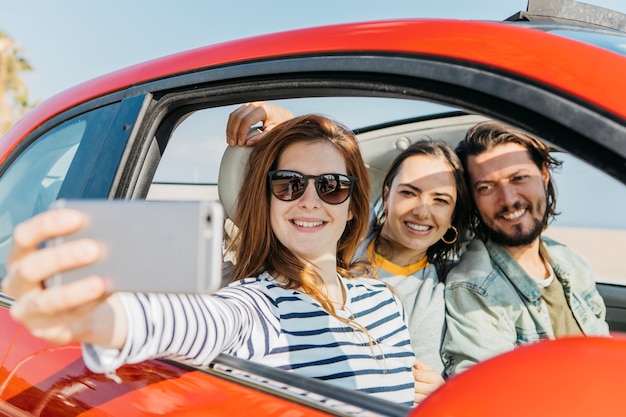 Women and positive man taking selfie on smartphone in car