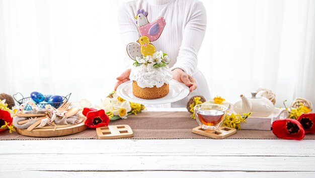 Women's hands are holding a festive Easter cake, decorated with flowers and bright details. The concept of preparing for the Easter holiday.