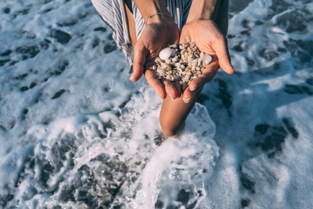 Women's hands are holding a lot of small pebbles