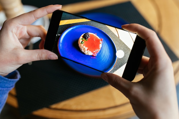 Free photo women's hands holding mobile phone, taking photo of tasty cake, served in plate.