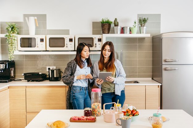 Women standing and watching tablet on kitchen