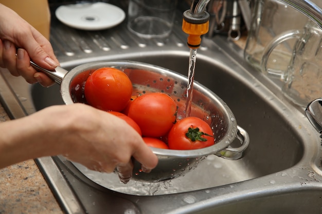 Free Photo a women using a colander and a kitchen sink to wash tomatoes.