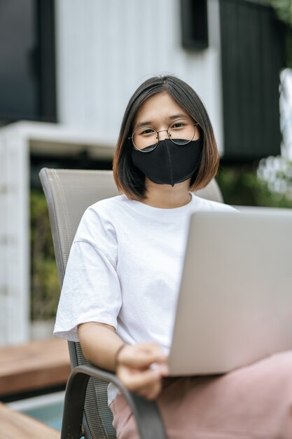 Women wearing masks and playing laptops at the poolside.