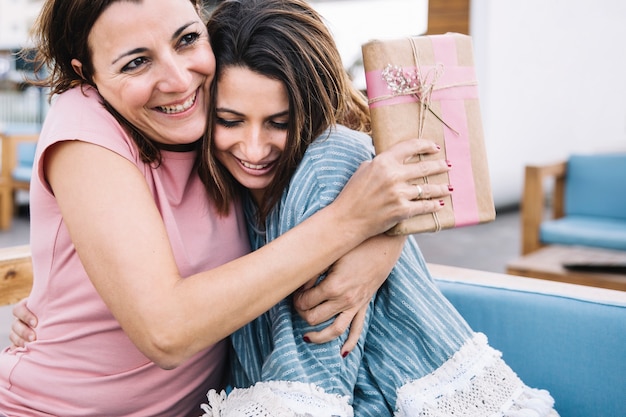 Free photo women with gift hugging on sofa