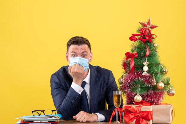 wondered man sitting at the table near xmas tree and presents on yellow