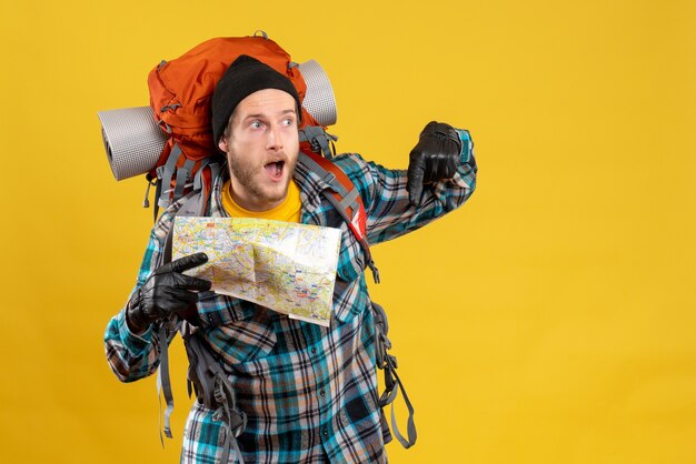 wondered young tourist with leather gloves and backpack holding map pointing at floor