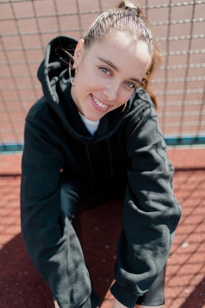 Free photo wonderful pretty lady with dark hair wearing dark pullover is sitting on sport square and looking up into the camera with happy emotions