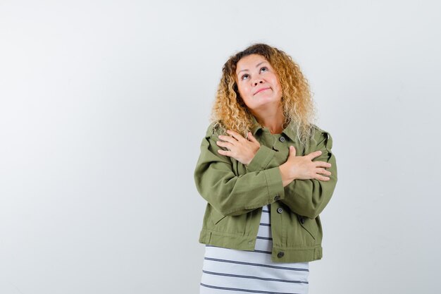 Wonderful woman in green jacket, shirt hugging herself and looking preoccupied , front view.