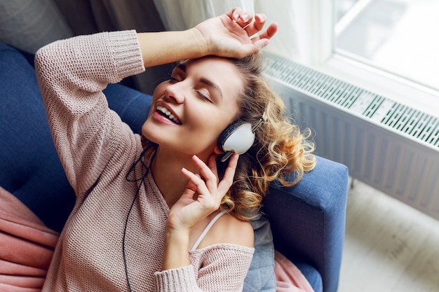 Free Photo wonderful woman with curly short hairs listen favorite music and lying  with closed eyes with pleasure. wearing  cute pink  loungewear.