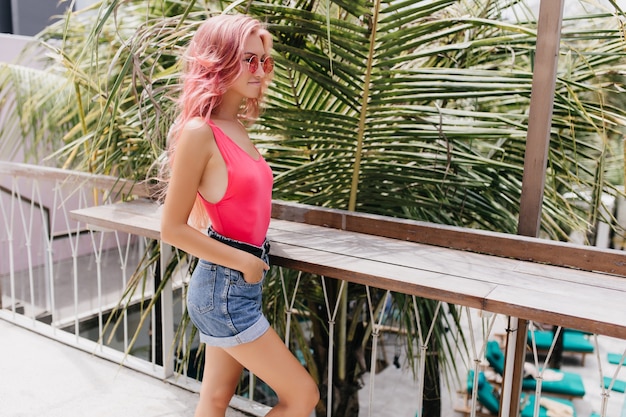 Free photo wonderful young woman in stylish summer outfit posing on exotic background.