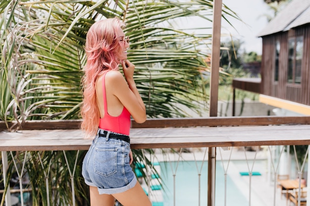 Free photo wonderful young woman in stylish summer outfit posing on exotic background.