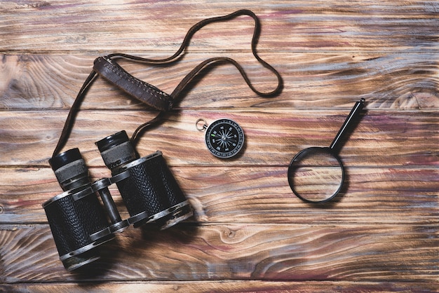 Free photo wooden background with binocular, compass and magnifying glass