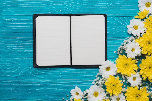 Wooden background with open notebook and flowers