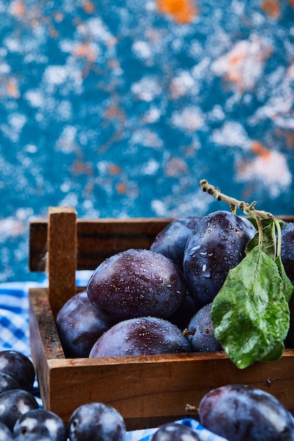 Free photo wooden basket of fresh plums on blue.