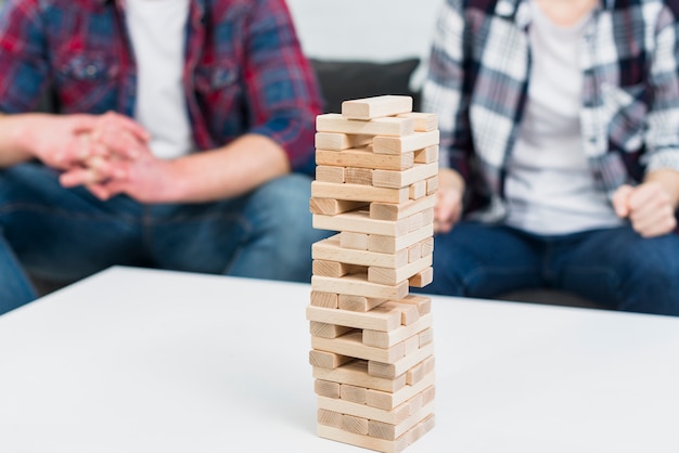 Free photo wooden block tower on white table in front of couple sitting on sofa