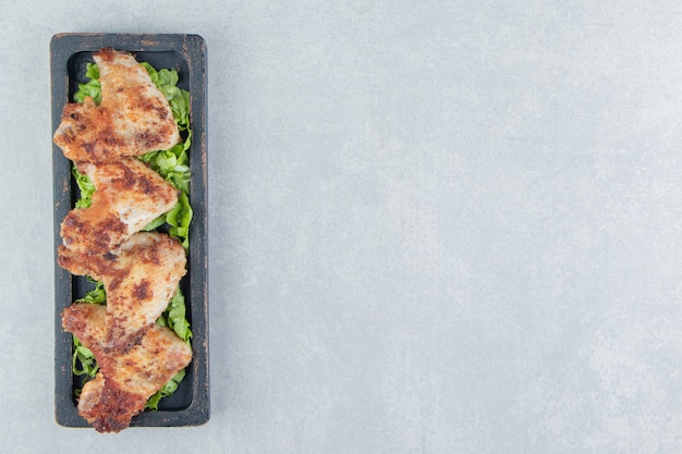 Free photo a wooden board of chicken fried meat with lettuce .