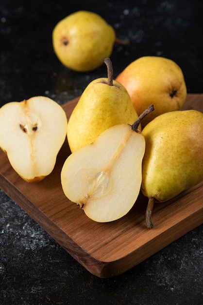 Wooden board of delicious yellow pears on black surface. 