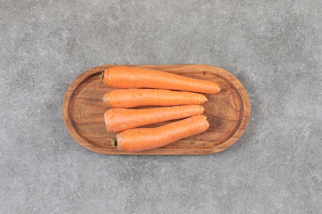 A wooden board of fresh sweet carrots placed on a stone surface.