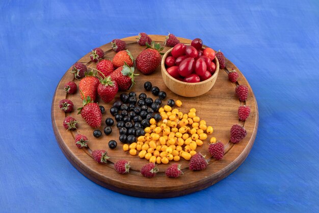 A wooden board full of berries on blue surface