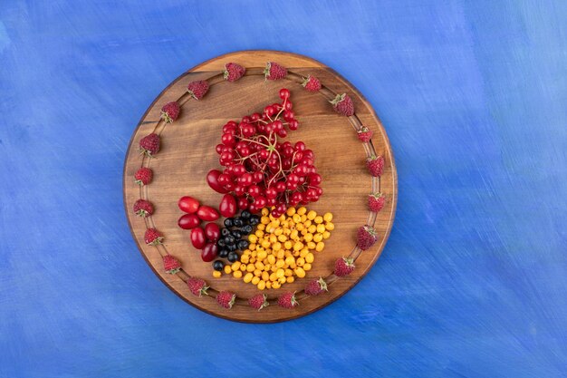 Free Photo a wooden board full of berries on blue surface