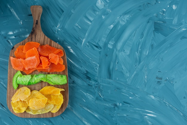 Wooden board full of dried fruits on blue background.