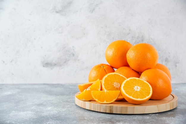 A wooden board full of juicy slices of orange fruit on stone table .