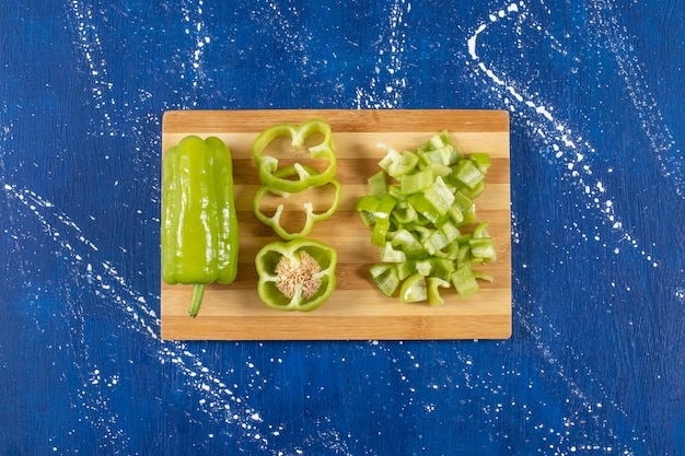 Free photo wooden board of sliced green bell peppers on marble surface