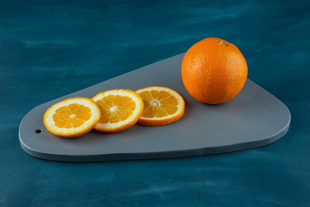 Wooden board of sliced juicy oranges on blue surface.