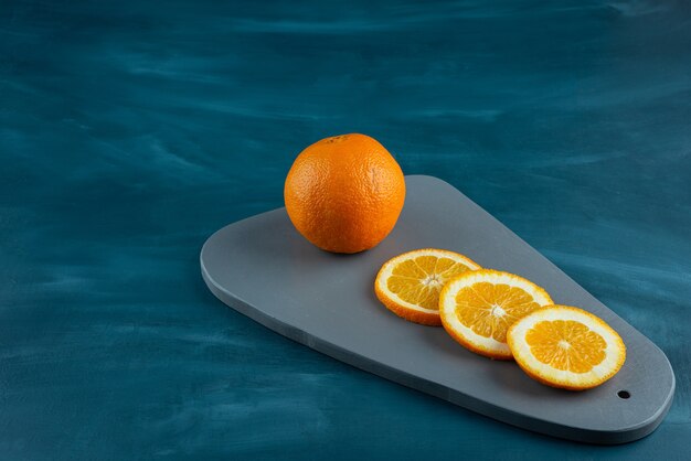 Wooden board of sliced juicy oranges on blue surface.