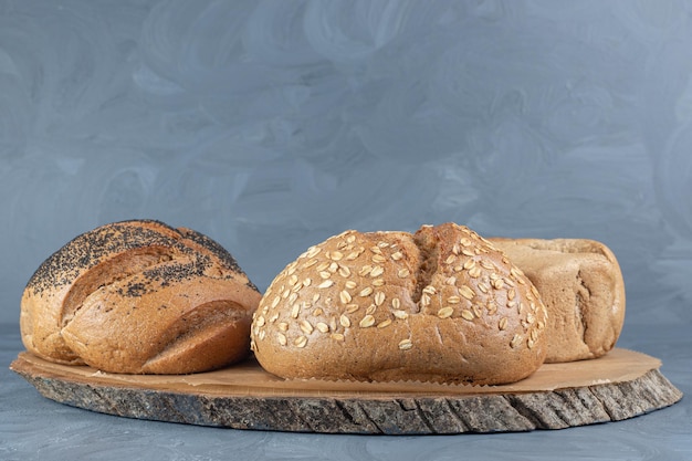 Wooden board under three loaves of bread on marble table.