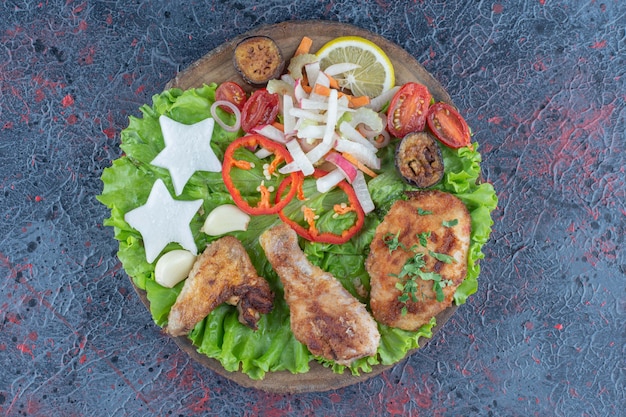 A wooden board with baked chicken meat and vegetables . 