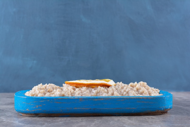 A wooden board with delicious oatmeal and a slice of orange fruit. 