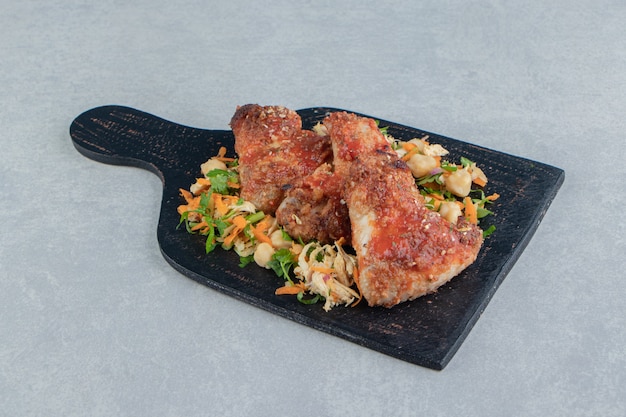 A wooden board with fried meat and vegetable salad .