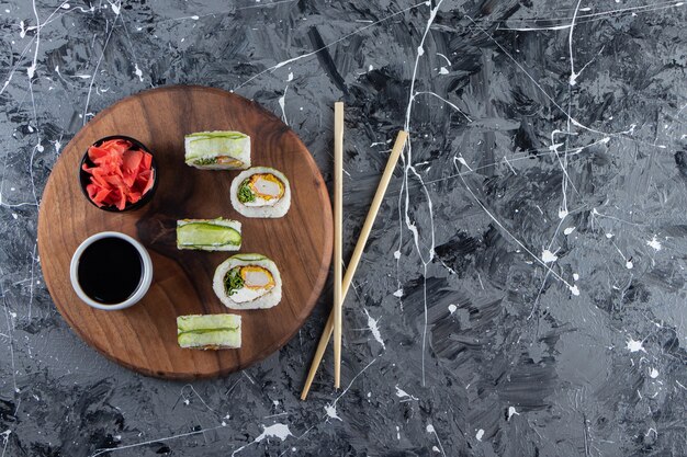 Wooden board with green dragon sushi rolls on marble background. 