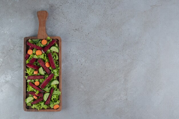 A wooden board with vegetable salad on a gray background. High quality photo