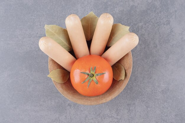 A wooden bowl of boiled sausages with red tomato and bay leaves 