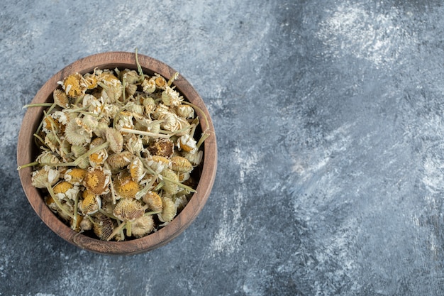 Wooden bowl of dried chamomile on marble table. 