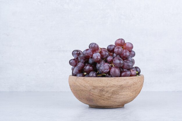 A wooden bowl full of purple grapes on white