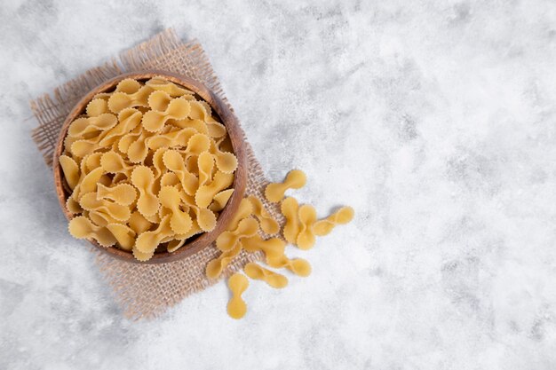 Wooden bowl full of raw dry Farfalle pasta placed on marble table . High quality photo