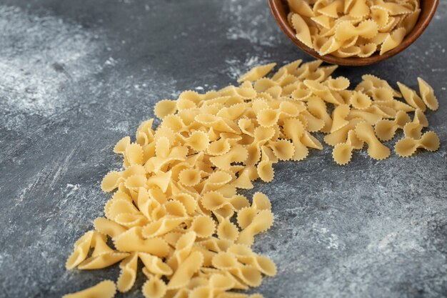 A wooden bowl full of raw farfalle tonde macaroni . 