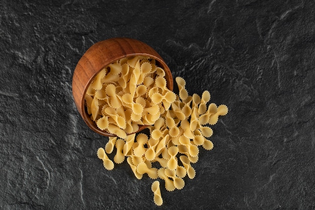 A wooden bowl full of raw farfalle tonde macaroni . 