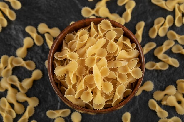 A wooden bowl full of raw farfalle tonde macaroni . 