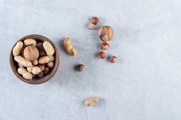 Wooden bowl full of various shelled nuts on stone background.