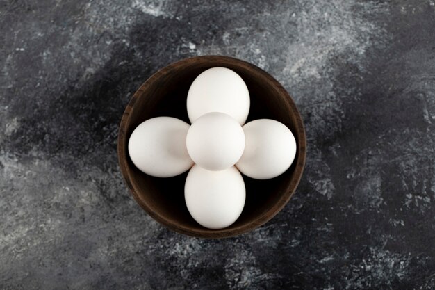 A wooden bowl full of white raw chicken eggs . 